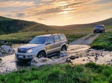 Off-road 4x4 crossing a river at sunset