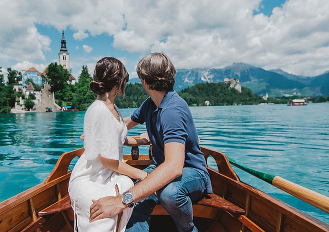 Couple on a wooden boat on Lake Bled with the island church and mountains