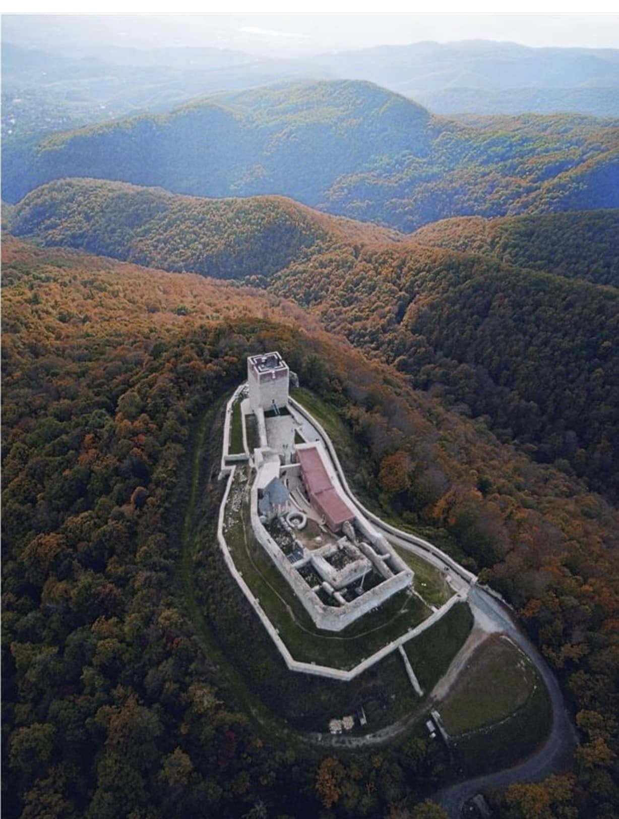 Aerial view of a hilltop fortress amid autumn forest